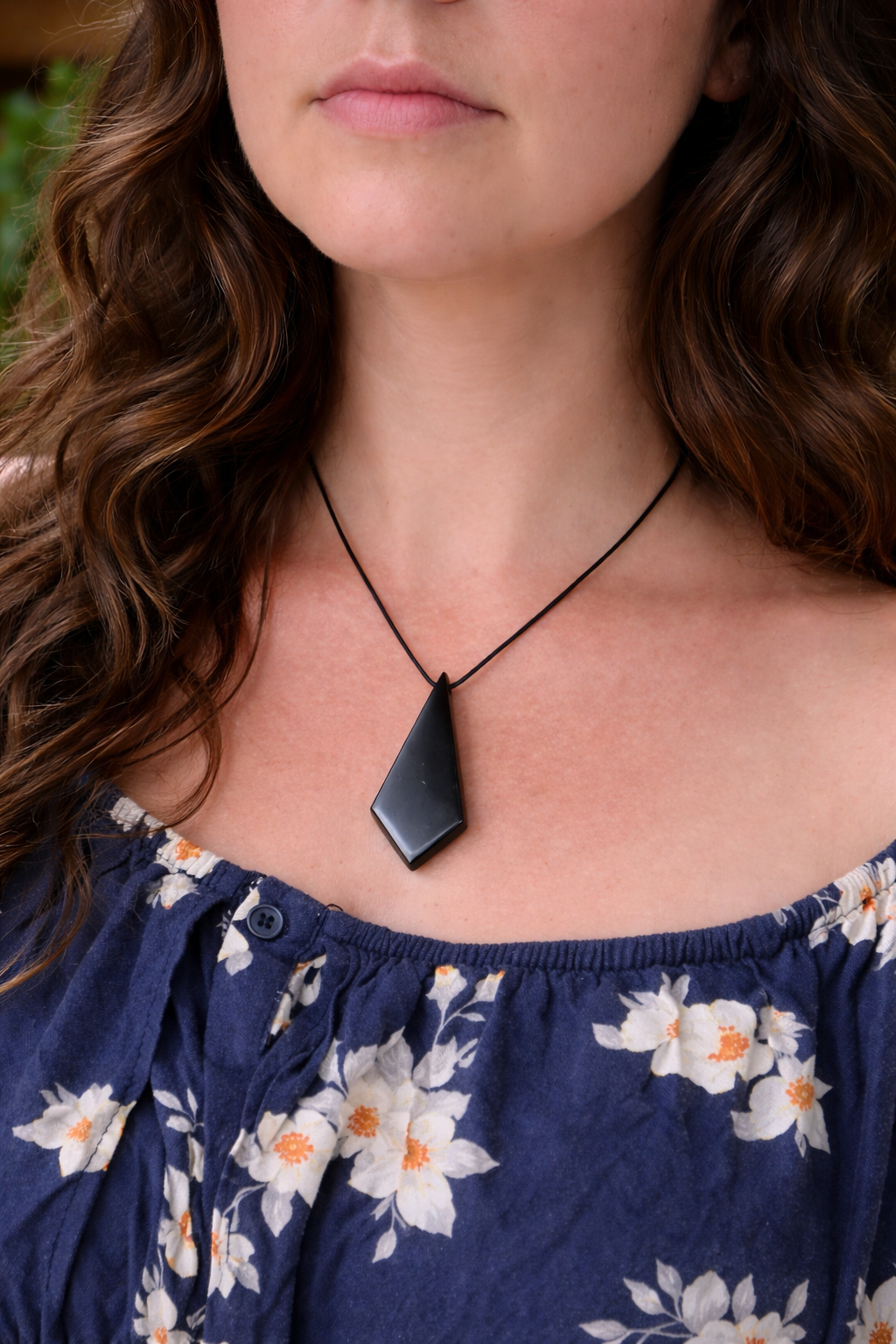 Close-up of a woman wearing a polished black shungite pendant on a simple black cord, styled in a soft boho look with natural lighting highlighting the stone’s smooth surface and geometric shape.