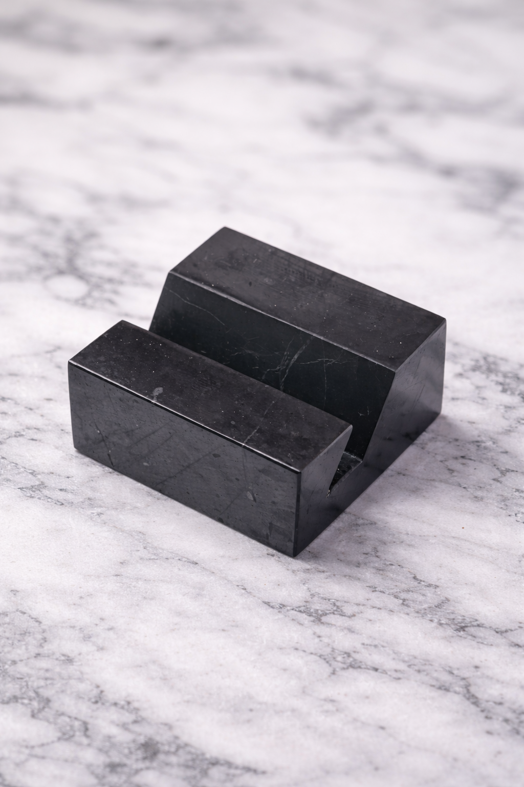 Shungite phone holder stand on white marble surface with soft natural lighting, showcasing a minimalist black stone design for desk organization and EMF protection