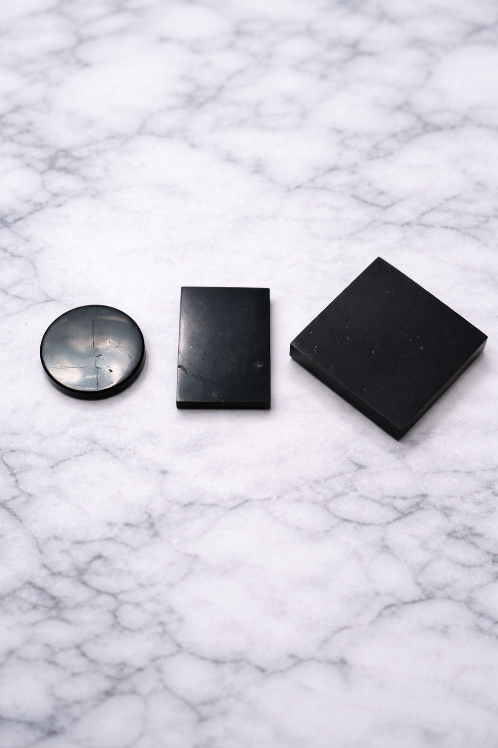 Set of three shungite phone plates including round, rectangular and square shapes on marble background