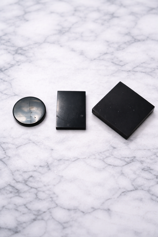 Set of three shungite phone plates including round, rectangular and square shapes on marble background