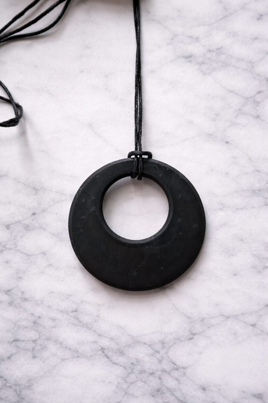 Round shungite pendant necklace on black cord displayed on white marble background