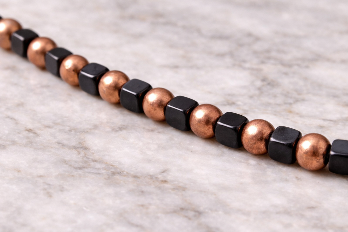 Close-up of handmade shungite cube and copper bead necklace on a light marble surface with soft natural lighting