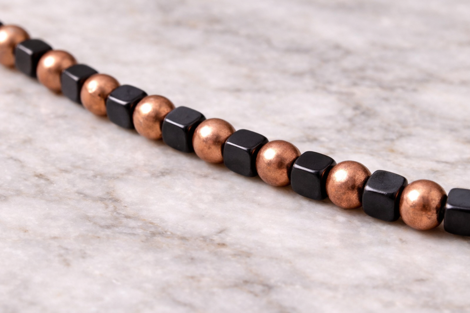 Close-up of handmade shungite cube and copper bead necklace on a light marble surface with soft natural lighting