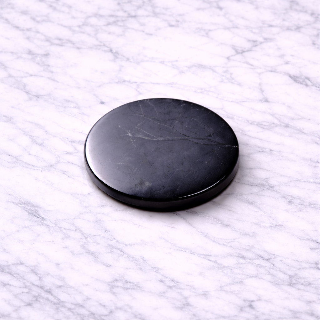 Polished black shungite EMF protection plate (30mm) resting on a white marble surface, showing natural stone veining and smooth glossy finish.