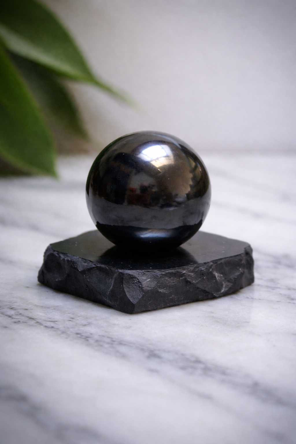 “Polished shungite sphere on rough stone stand placed on white marble surface”