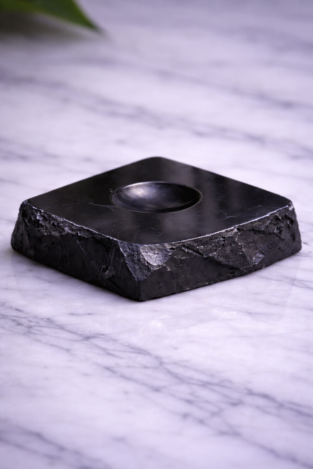 “Polished black shungite sphere stand with small center groove on white marble”