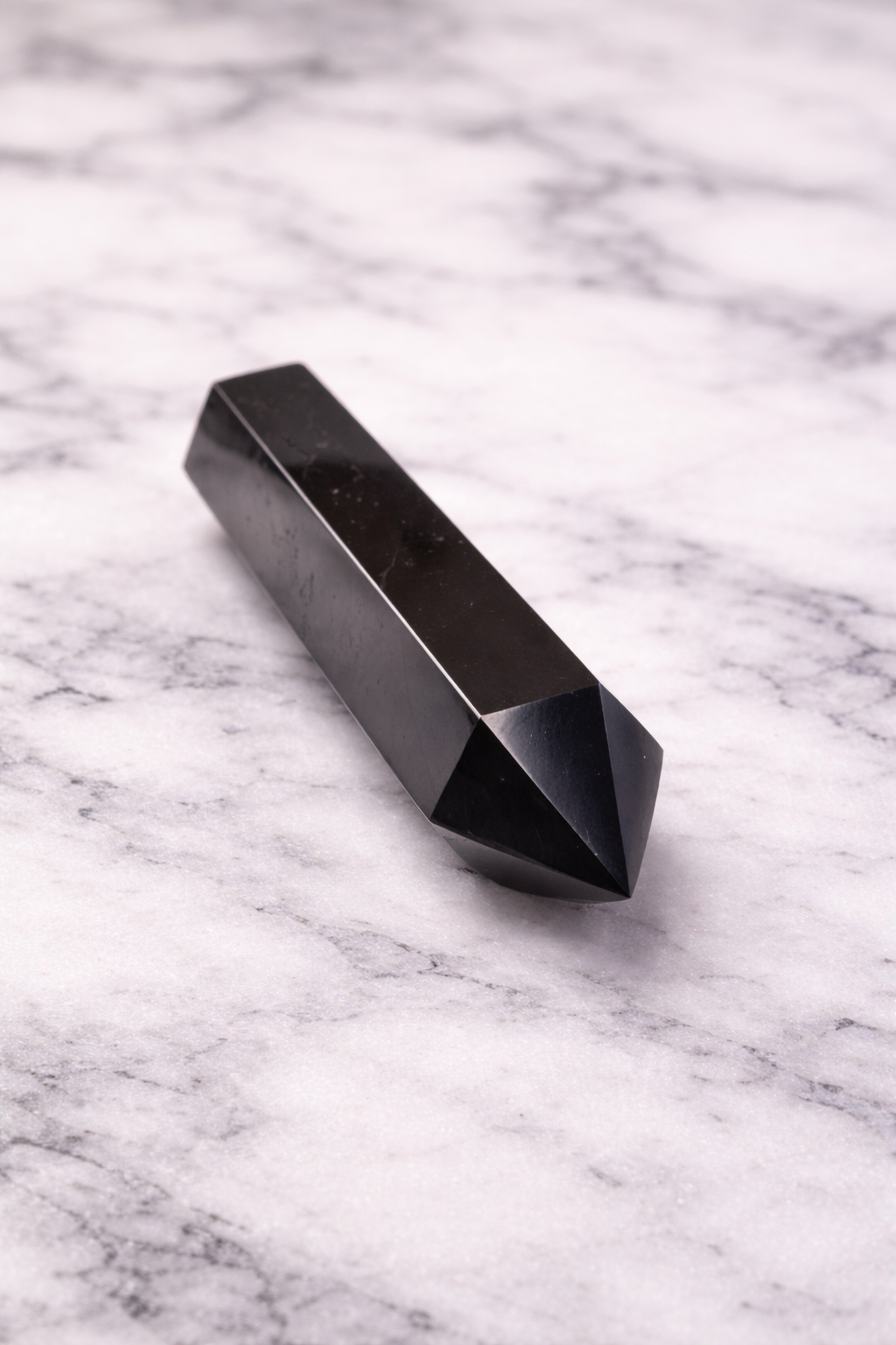 Polished shungite crystal wand with pointed tip on white marble background