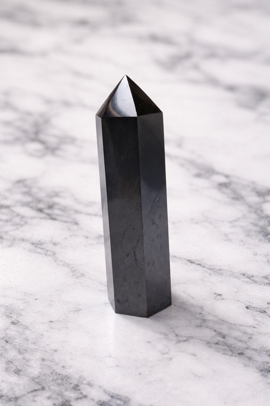 Polished shungite crystal tower point standing on white marble background