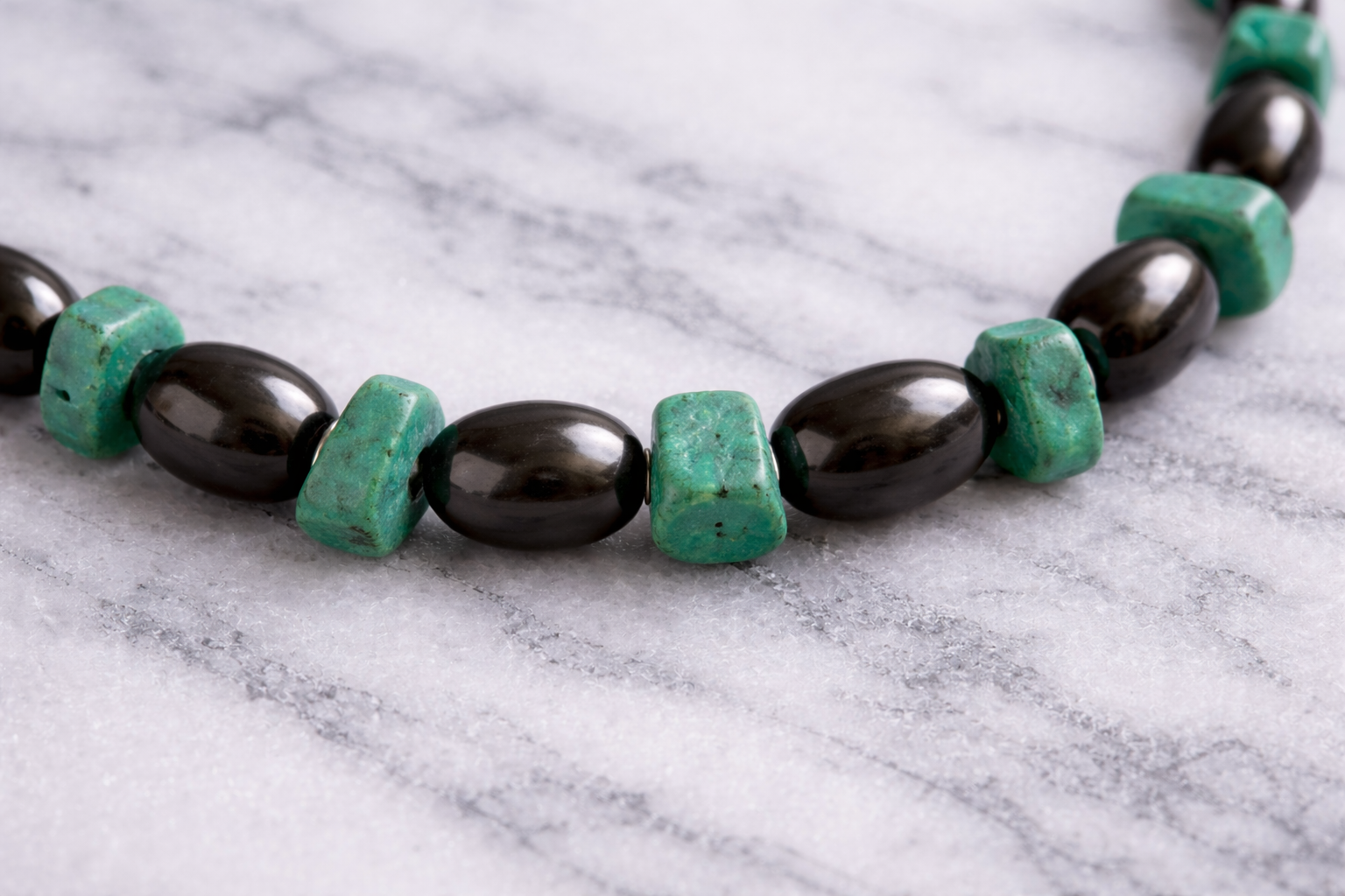 Close-up of alternating raw turquoise stone and black polished  shungite beads necklace on white marble surface 