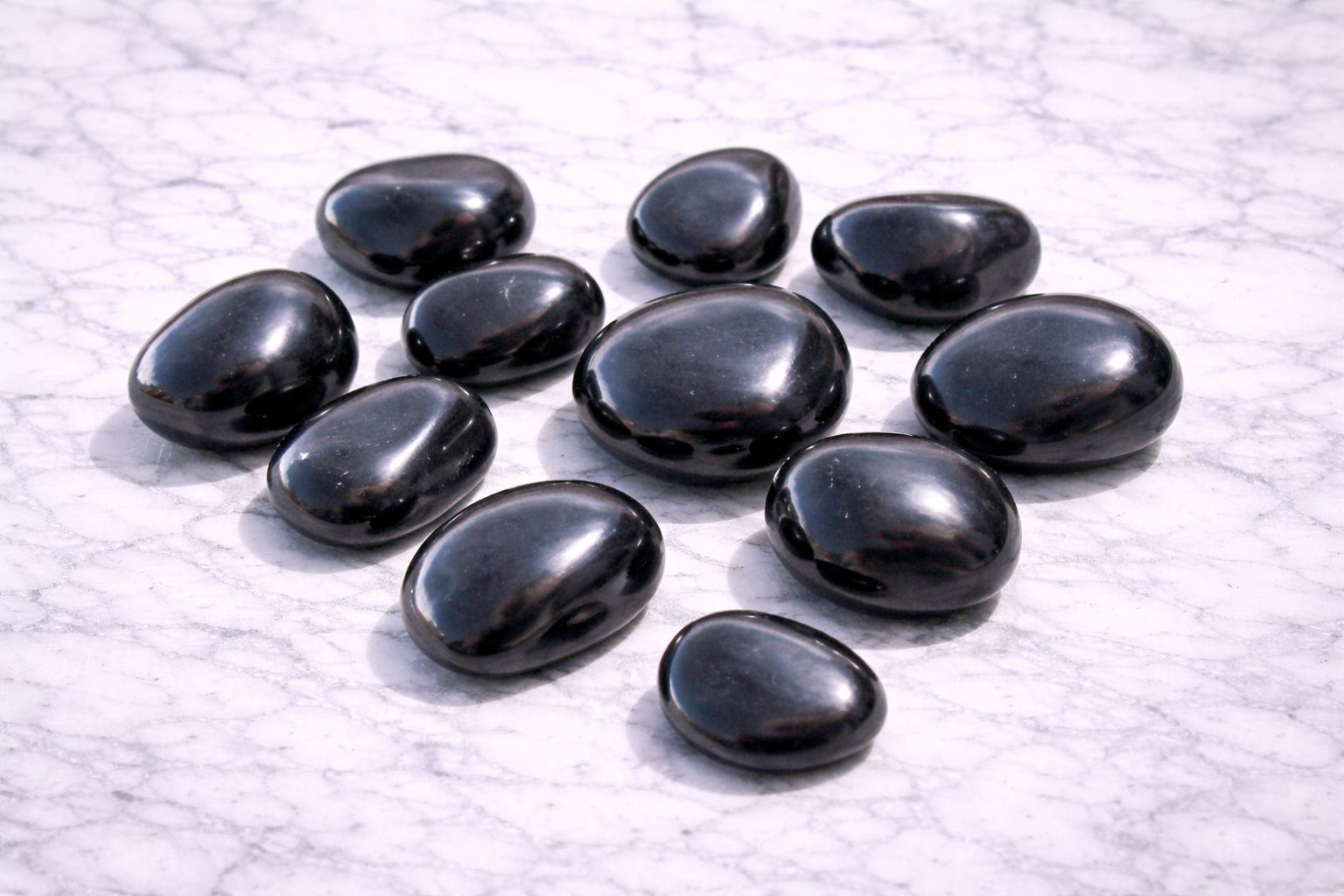 Scattered polished shungite stones on a white marble surface, showing smooth black tumbled crystals with a glossy natural shine.